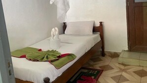 A single bed with a canopy, a wooden headboard, a bedside table with a white towel, and a red and green mat on the floor. - Jungle Green Resort - Kiutine (Maua)