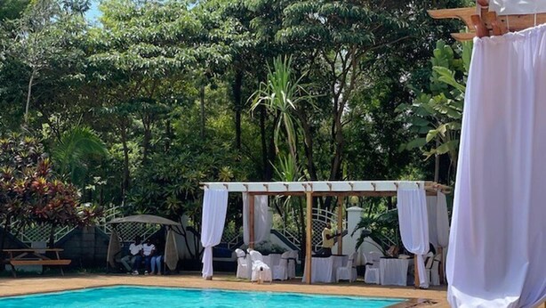 A swimming pool with a person in the water, surrounded by lush greenery and a covered seating area. - Jungle Green Resort - Kiutine (Maua)
