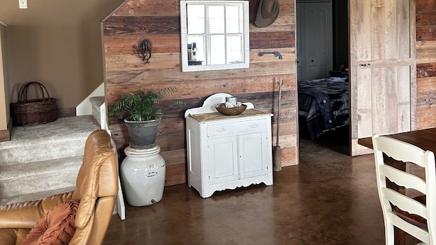 A rustic interior with a loft-style bedroom, a dining area, and a living space with a concrete floor.