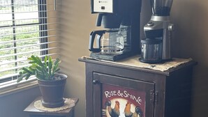 A coffee maker on a cabinet with a rooster decoration and a potted plant.