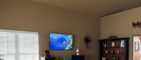 A living room with a television, a bookshelf, and a window with blinds.