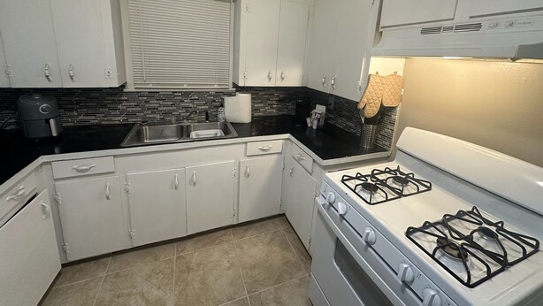A kitchen with white cabinets, a black countertop, a gas stove, and a window with blinds. - Workers Special 1.7 Miles From CP Chem Project (West Orange)
