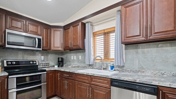 Una cocina con armarios de madera, electrodomésticos de acero inoxidable, encimera de granito y una ventana con persianas.