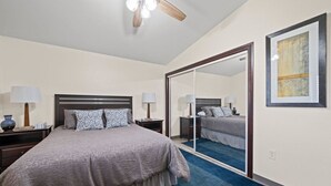 Un dormitorio con una cama grande, un ventilador de techo, un espejo y una obra de arte enmarcada en la pared.