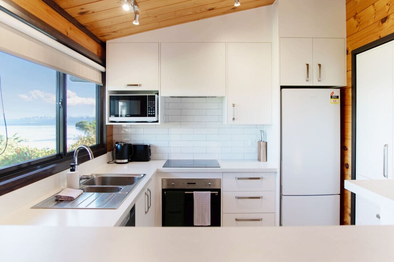 Une cuisine moderne avec des armoires blanches, un four à micro-ondes, une cuisinière, un évier et un réfrigérateur.