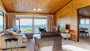 Una sala de estar moderna con sofá, sillón y televisor, paredes de madera y un ventanal con vistas.