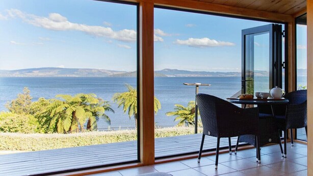 Una habitación con un gran ventanal, una mesa con sillas y vistas al mar y a las montañas.