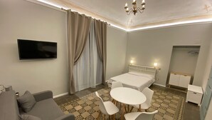 Une chambre d’hôtel comprenant un lit, une télévision, une table à manger avec des chaises, un canapé et un sol à motifs.