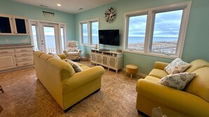 A living room with two yellow sofas, a TV, and a view of the ocean.