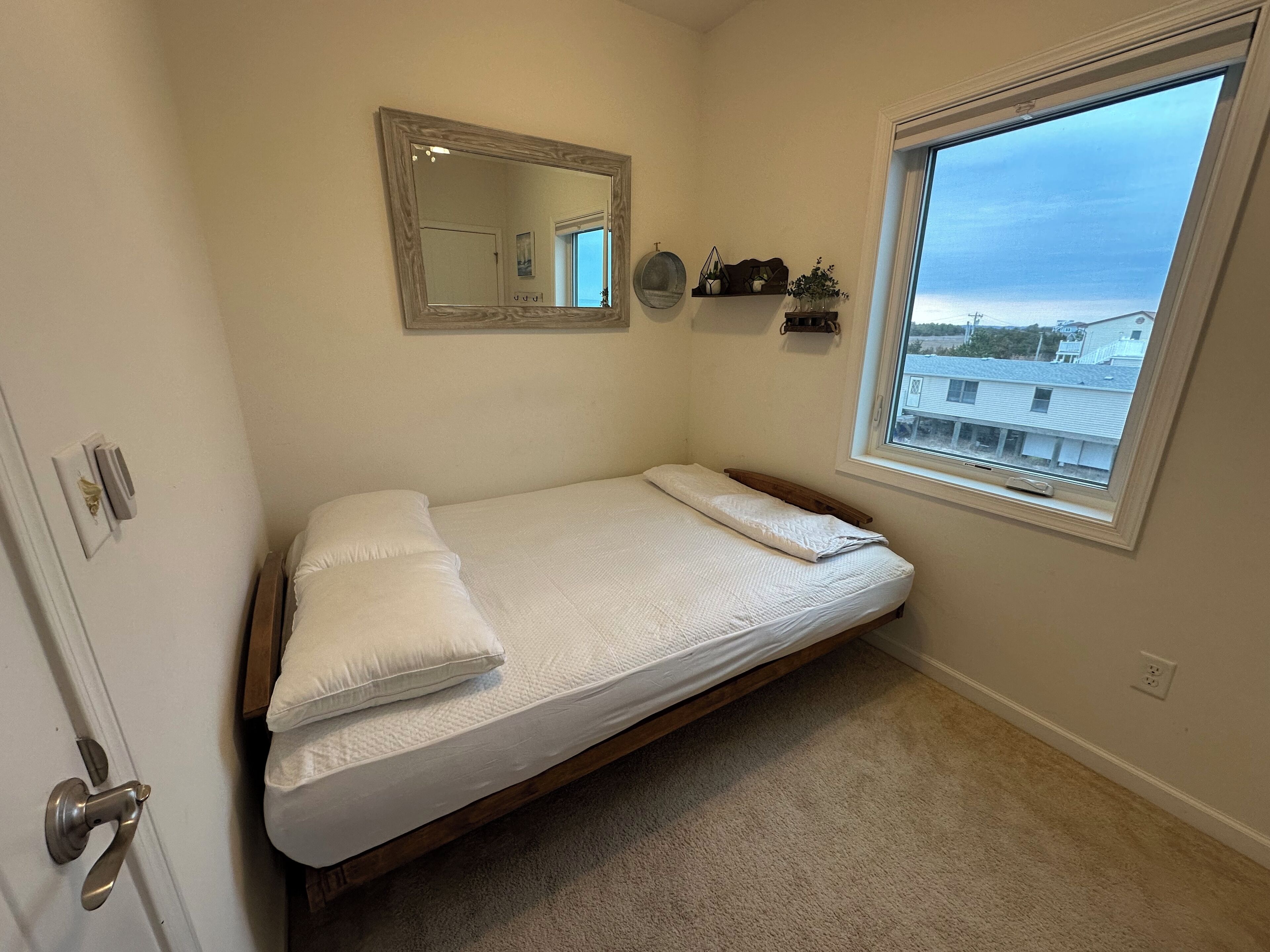Une petite chambre à coucher avec un lit simple, une fenêtre, un miroir et une porte.
