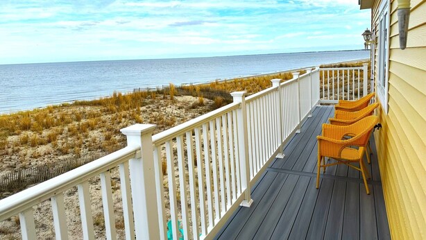 A wooden deck with white railings overlooking a beach.