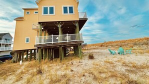 A two-story house with a balcony, wooden deck, and beach chairs.