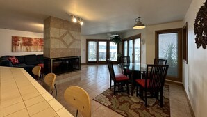 A spacious living area with a dining table, chairs, and a fireplace. There is a large window providing natural light and a view of the outdoors. - Experience lakefront luxury with spectacular views on Lake James, Indiana! (Angola)