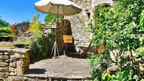 Une cour pavée de pierres, avec un banc en bois, un trépied et un grand parasol.