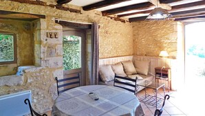 Un intérieur rustique en pierre, avec une table ronde, des chaises, un banc rembourré et une petite table sur laquelle se trouve une lampe.