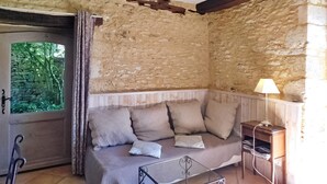 Une pièce chaleureuse avec un mur en pierre, un banc en bois, une table en verre et une lampe.
