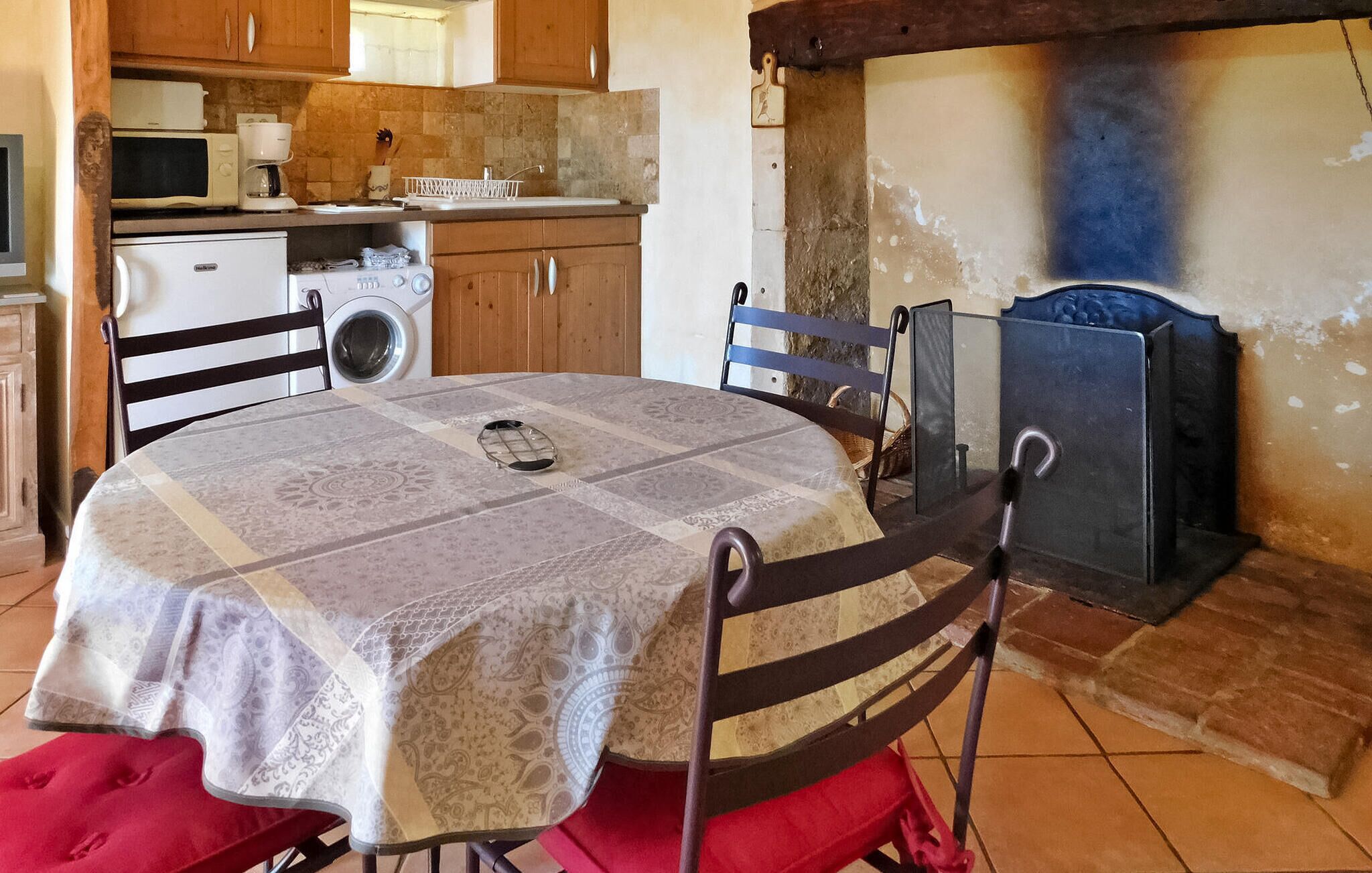Una cocina con mesa, sillas, lavadora, microondas y horno de leña.