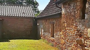 Un bâtiment en pierre avec un toit en tuiles et une cour couverte d’herbe.