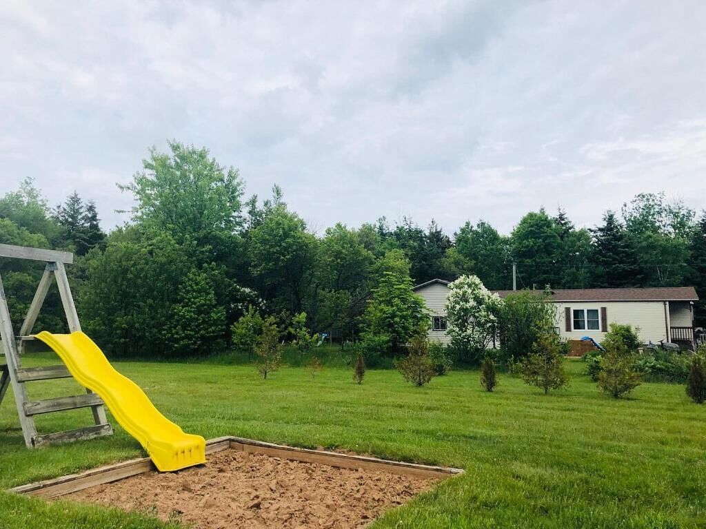 A backyard with a yellow slide, a wooden swing set, and a house in the background.