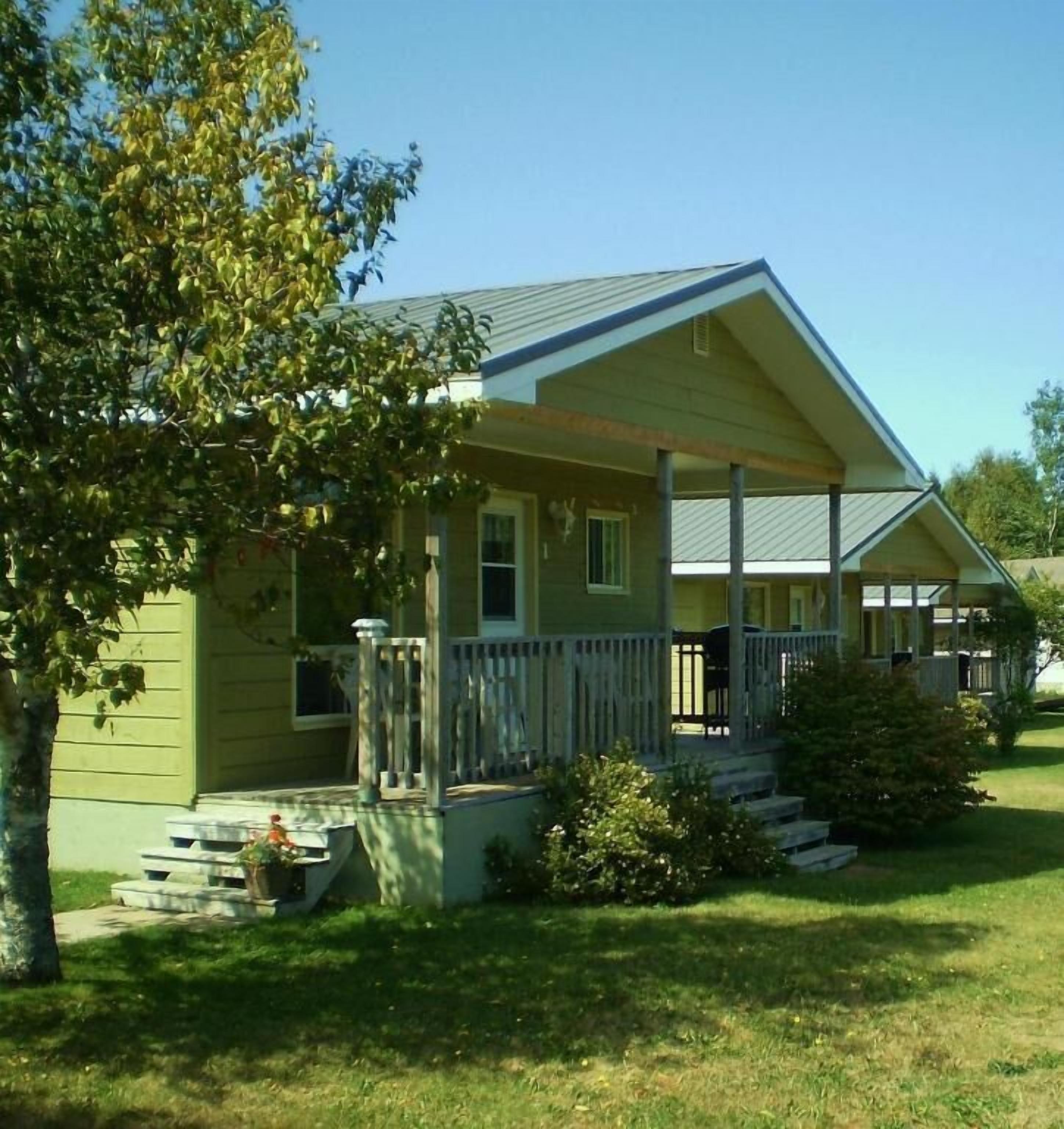 Een gelijkvloers huis met een veranda, een kleine voortuin en een boom links.