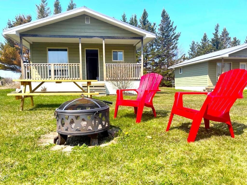 A lodge with a porch, a fire pit, and red chairs.