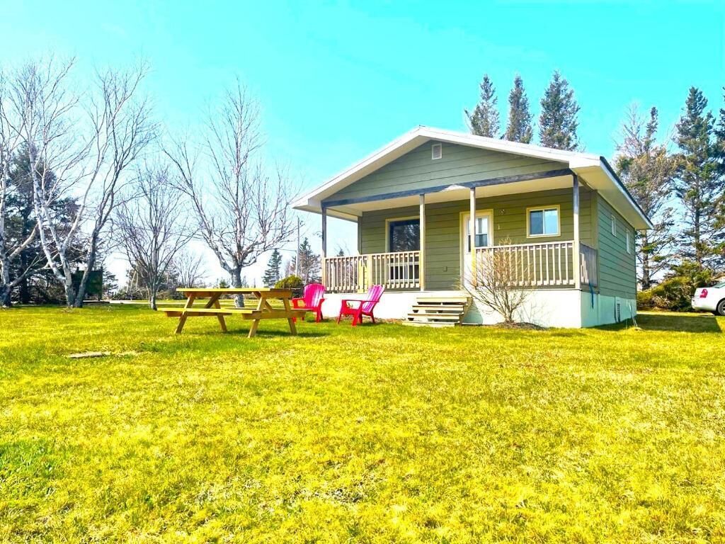A single-story house with a porch, a picnic table, and two red chairs.