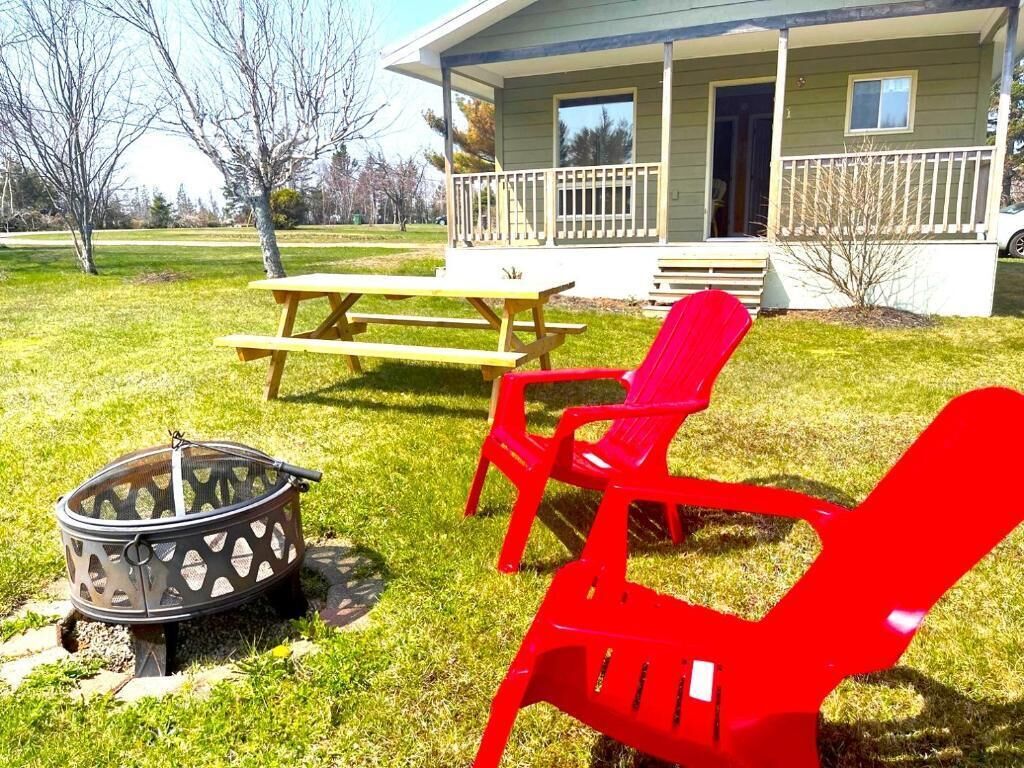 A backyard with a fire pit, picnic table, and red Adirondack chairs in front of a house with a porch.