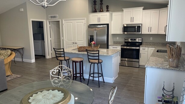 A modern kitchen with white cabinetry, a central island with bar stools, stainless steel appliances, and a chandelier. - New modern 3-bed 2 bath house with smart TV's in every room, WIFI, and hot tub (Fort Pierce)