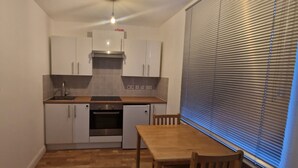 A compact kitchen with white cabinets, a small oven, and a wooden table. - Retreat Studio Camberwell zone 2 (London)