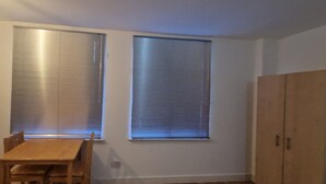 A small kitchen with a wooden table and chairs, two windows with blinds, and a wooden cabinet. - Retreat Studio Camberwell zone 2 (London)