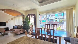 Una sala de estar con sofá, televisor y comedor con mesa de vidrio y sillas.