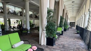 A covered outdoor area with green seating, potted plants, and a brick floor.
