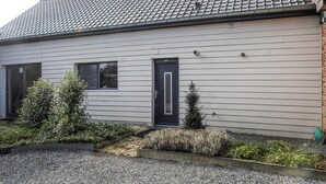 Une maison de plain-pied avec une porte de couleur foncée, deux fenêtres et un toit recouvert de tuiles.