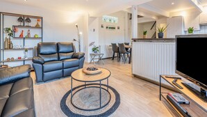 Un salon moderne avec un canapé en cuir noir, une table basse en bois et un téléviseur posé sur un meuble en bois.