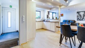 Une chambre d’hôtel moderne dotée d’une kitchenette, d’un coin repas avec une table et des chaises, et d’un espace de détente avec un canapé et un tableau au mur.