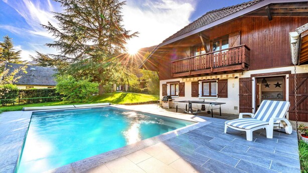 A pool area with a wooden deck, lounge chairs, and a barbecue grill.