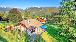 A chalet with a swimming pool, surrounded by lush greenery and mountains.