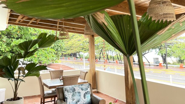 An outdoor patio with a wooden pergola, seating area with cushions, and potted plants. - Casa de la Playa (Puerto Plata)