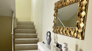 A staircase with a metal handrail leading to a landing. A white console table with a mirror and decorative items is positioned against the wall. - Casa de la Playa (Puerto Plata)