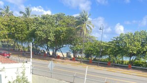 A poolside view with a wooden tray holding two cups, a clear blue pool, and a street with palm trees and a red car in the background. - Casa de la Playa (Puerto Plata)