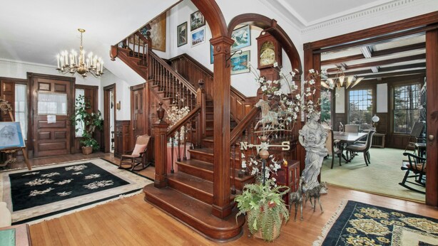 A grand staircase with wooden railings and a chandelier, surrounded by potted plants and a statue. - 5 bdrm Victorian, built in 1881-With 21 rooms, on a hill on 4 VERY private acres (New Windsor)