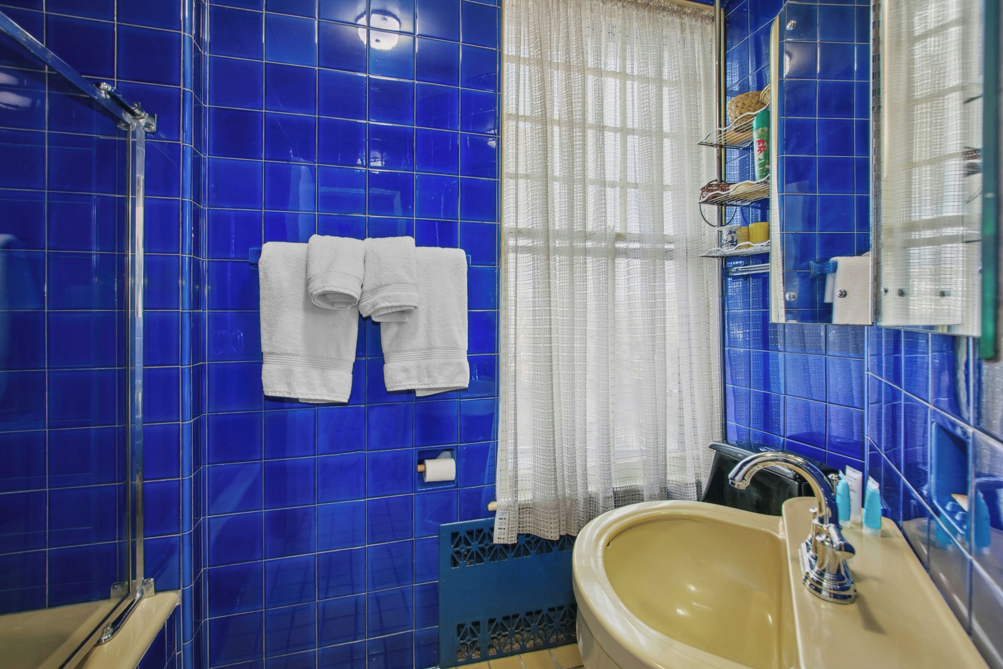 Casa de banho com azulejos azuis, uma pia, um espelho e duas toalhas penduradas na parede.