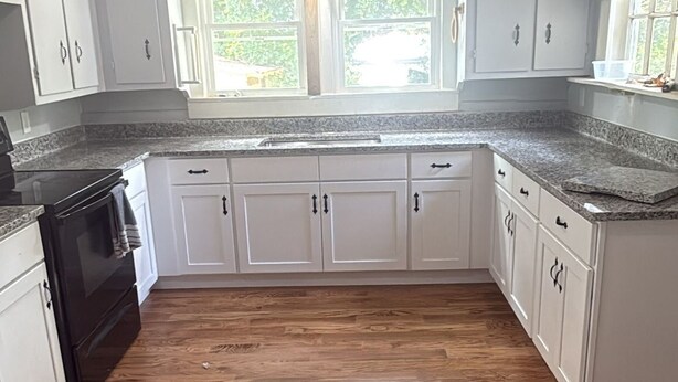 A kitchen with white cabinets, a granite countertop, and a black stove. - Cute cottage in a rural setting (Clemmons)