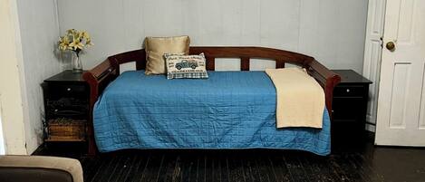 Un dormitorio con cama, mesita de noche, cómoda, silla y una mesa de centro con una planta.