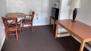 A small room with a round wooden table, two wooden chairs, a single table lamp, a microwave, and a power outlet on the wall. - Royal A Motel (Auburn)