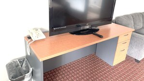 A hotel room with a wooden desk, a television, a remote control, a telephone, and a trash bin. - Royal A Motel (Auburn)