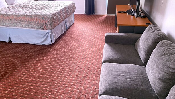 A hotel room with a bed, a grey sofa, a TV on a wooden table, and a red patterned carpet. - Royal A Motel (Auburn)
