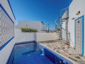 A swimming pool with a tiled edge, a staircase, and a white building with blue trim.