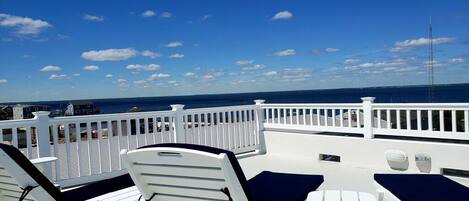 A deck with white lounge chairs and a white railing overlooking the ocean.