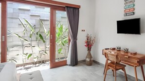 A modern room with a sliding glass door leading to a balcony, a wooden desk with a chair, a flat-screen TV mounted on the wall, and a decorative vase with flowers. - Belvilla Serene Haven Nusa Dua Beach (Nusa Dua)